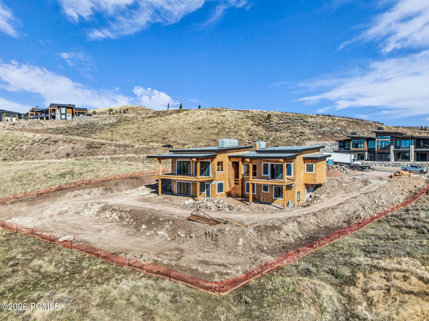 A two-story house under construction with wood siding on a hillside under a blue sky.