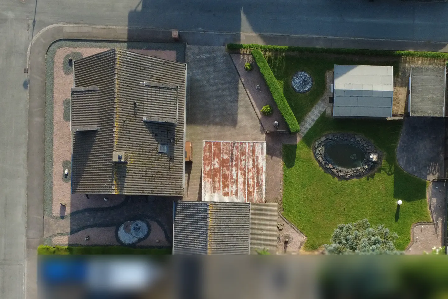 Aerial view of a house with a tiled roof, a paved driveway, a small garden pond, and a green lawn on a corner lot.