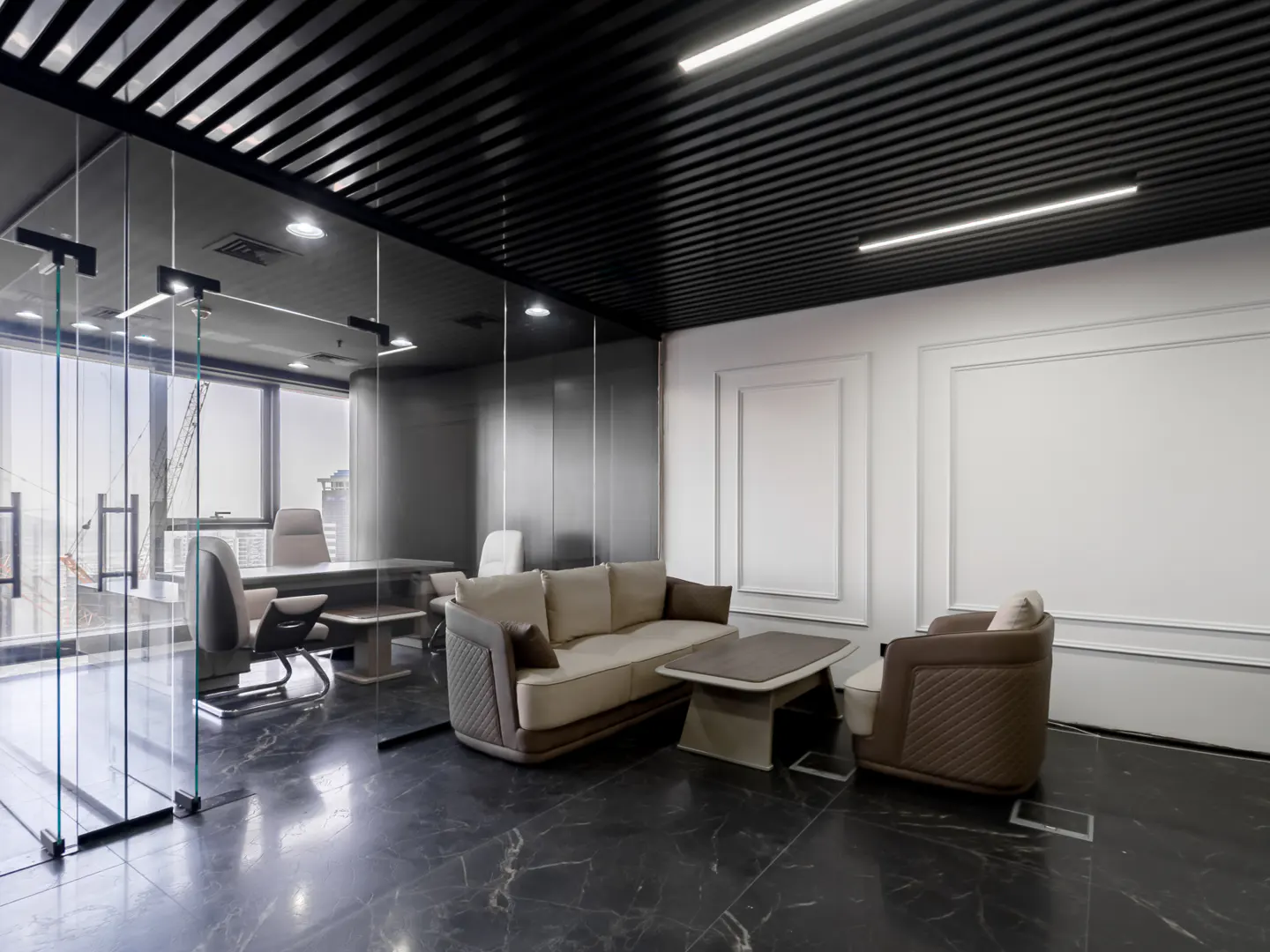 Modern office interior with glass walls, black marble floors, and a beige sofa and chair set. A desk and chairs are visible in the background.