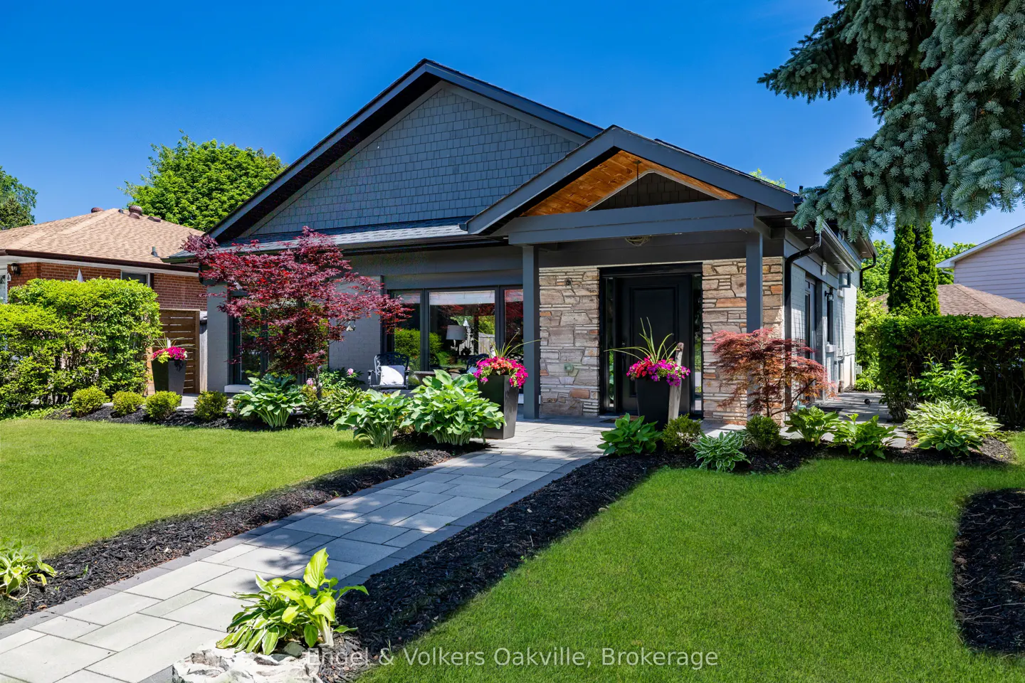Modern bungalow with grey siding, stone accents, and a stone walkway leading to the front door under a clear blue sky.