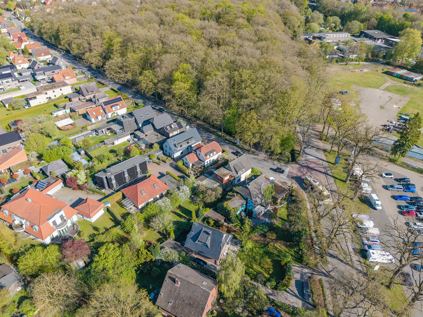 Aerial view of a residential area with houses, trees, and a parking lot on a sunny day.