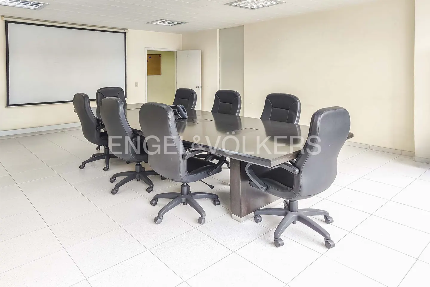 Conference room with a long table, black rolling chairs, and a projector screen on the wall.