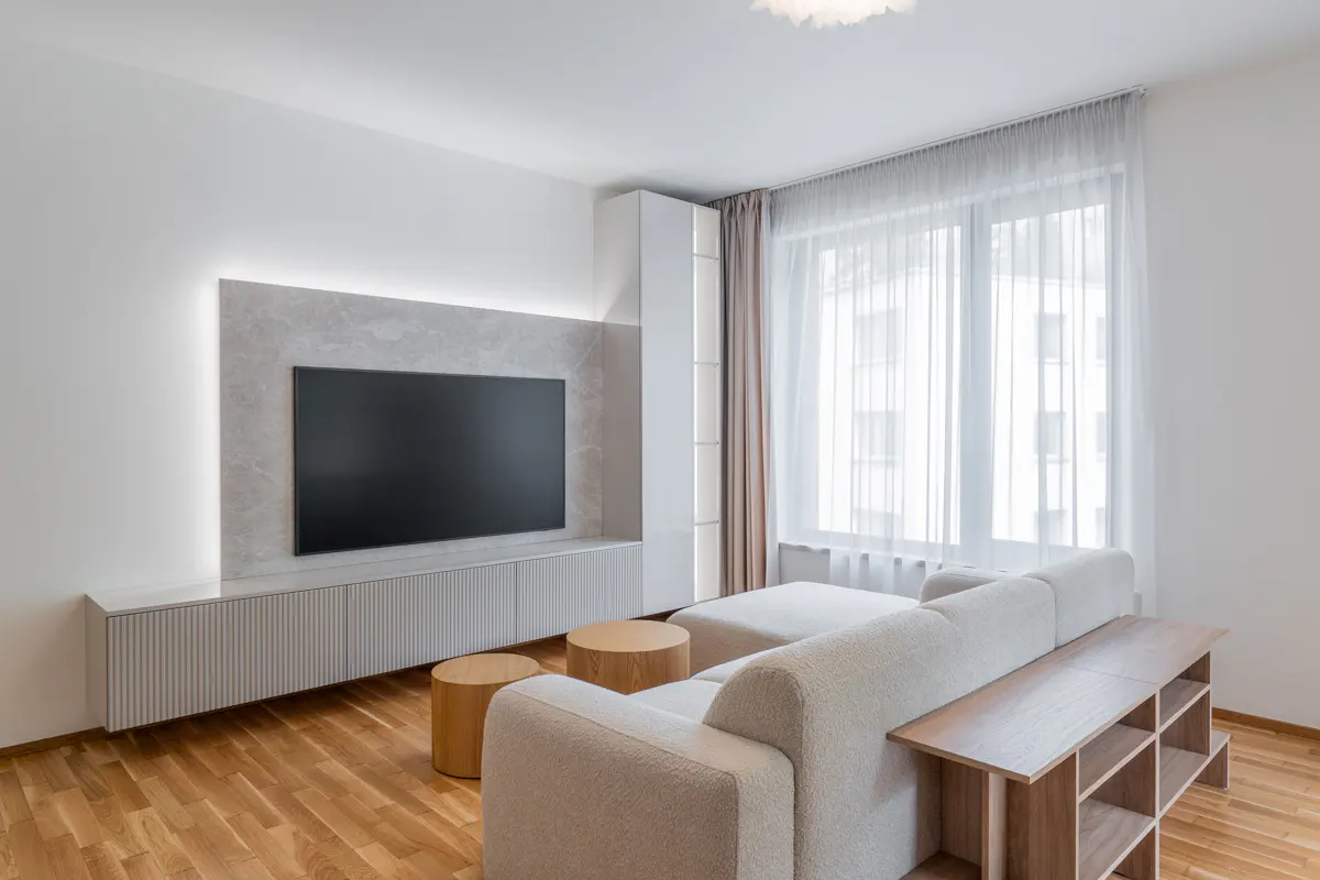 Bright living room with a white sectional sofa, wood floors, and a large TV mounted on a marble-look wall with LED lighting.