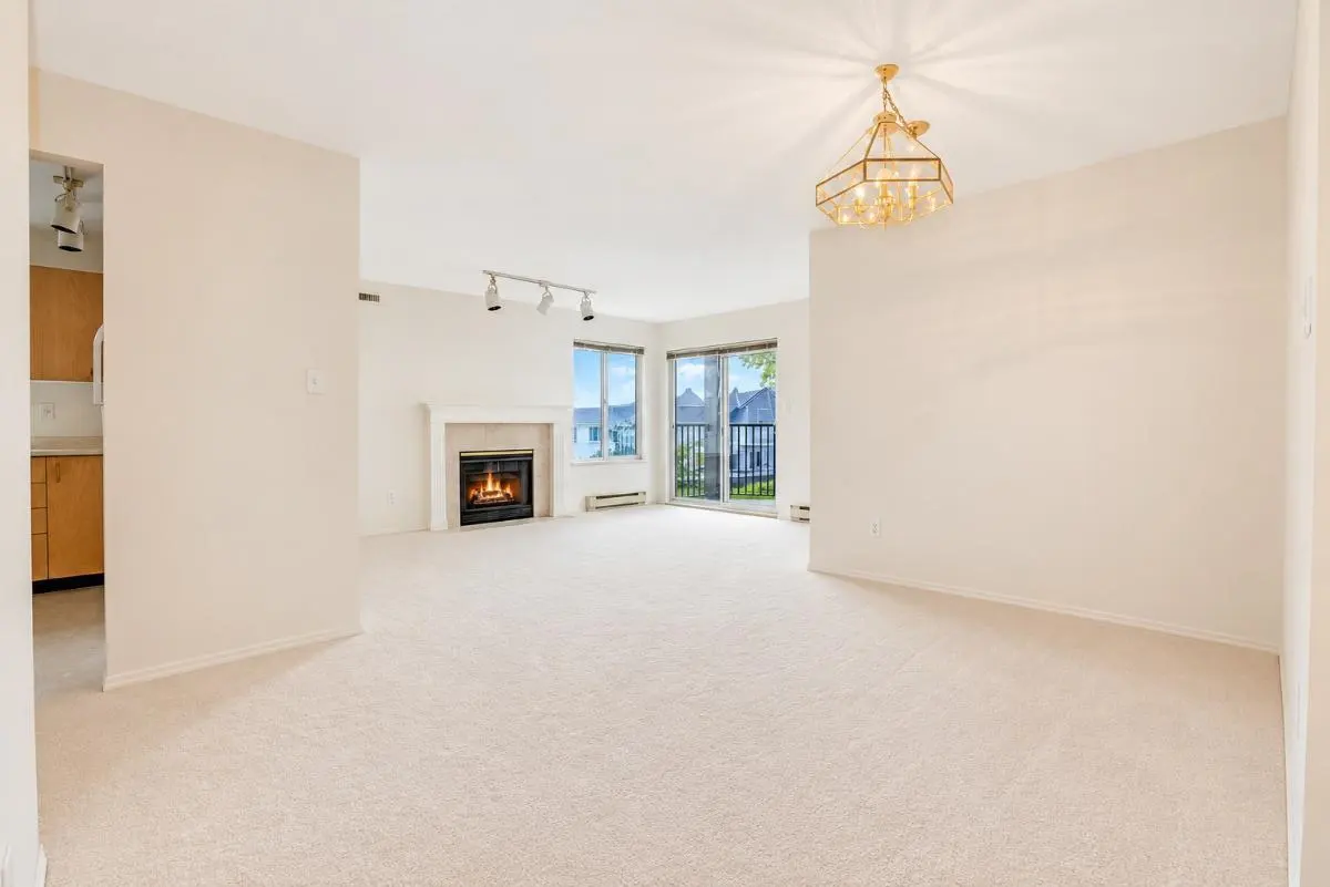 Bright living room with beige carpet, a fireplace, gold chandelier, and sliding glass doors leading to a balcony.
