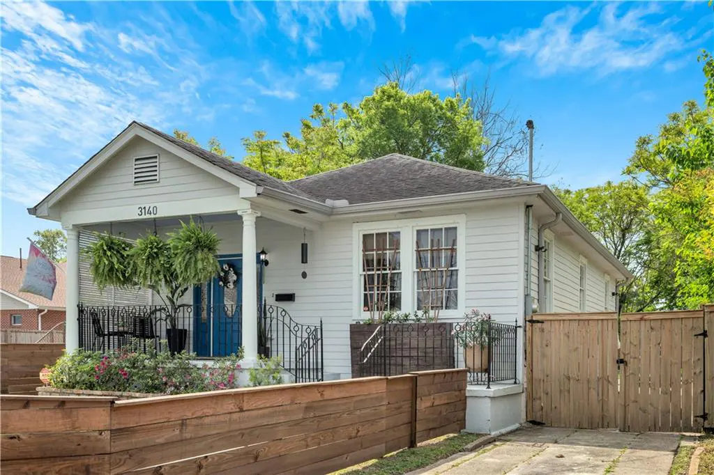 Exterior view of a white, single-story house with a blue front door and a wooden fence.