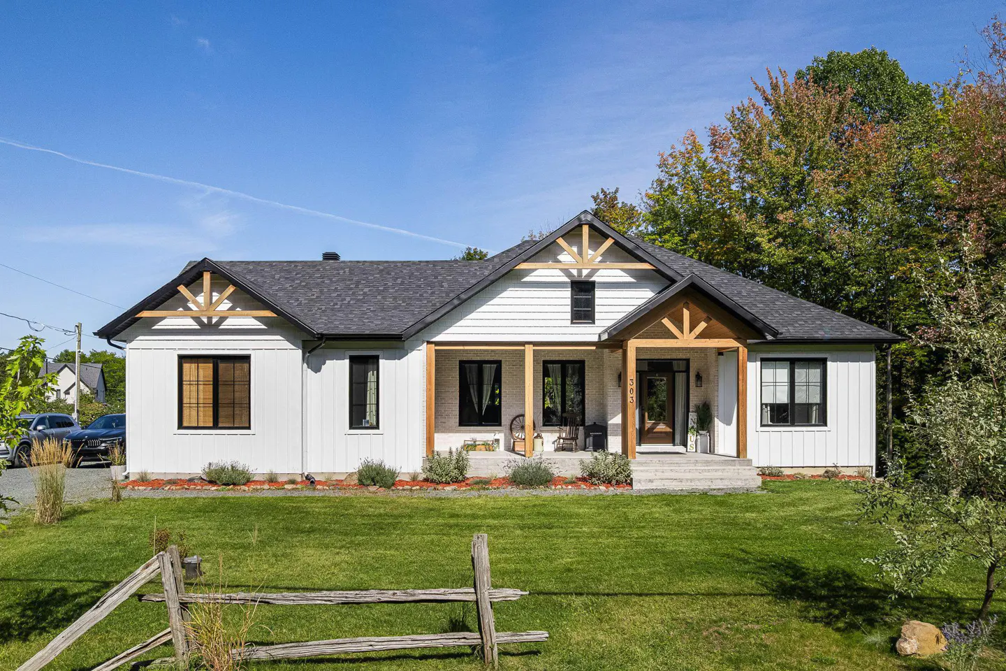 Exterior of a white farmhouse with black trim, a gray roof, and a green lawn under a blue sky.