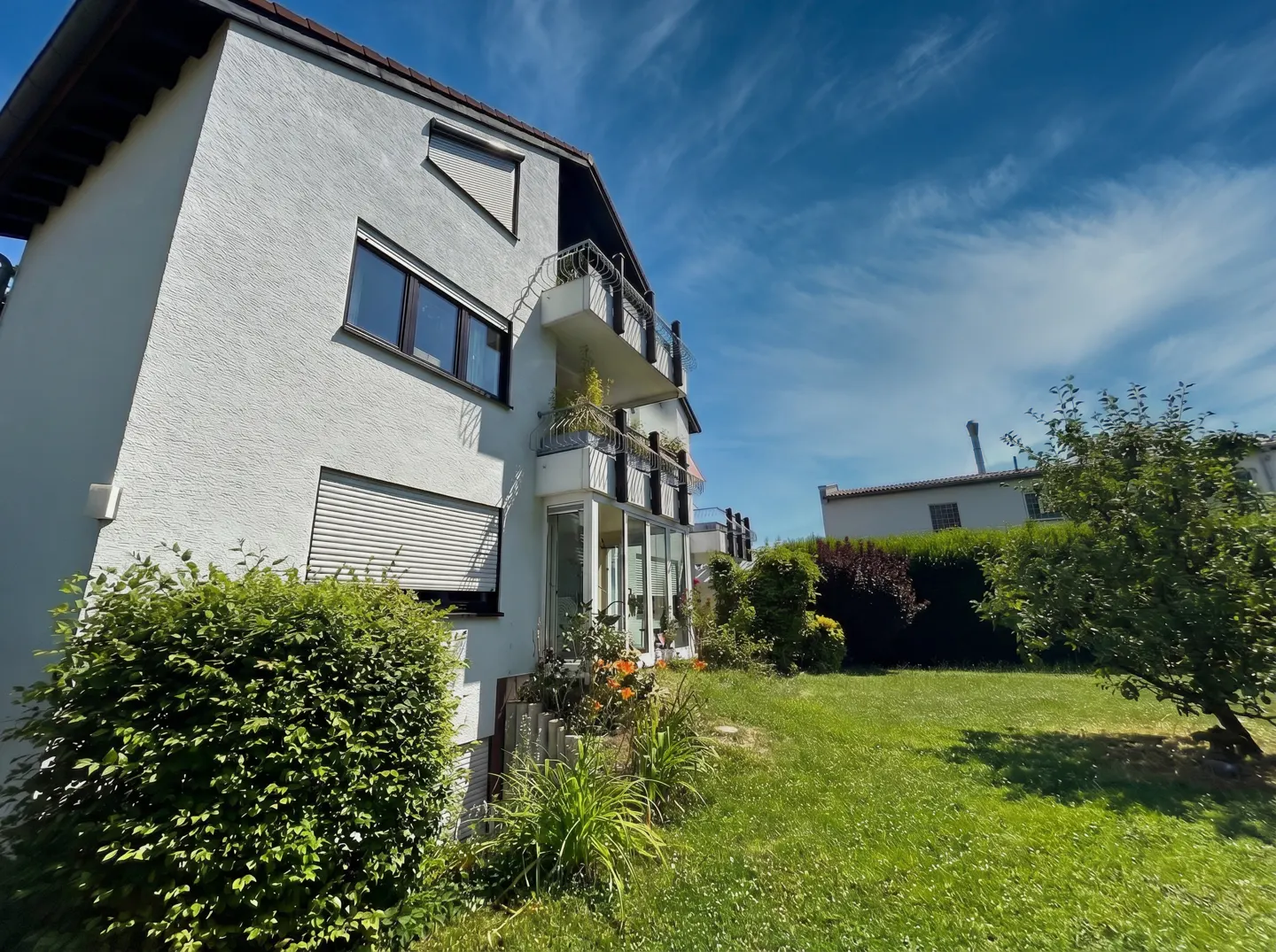 Exterior view of a white stucco house with balconies, windows, and a green lawn under a blue sky.