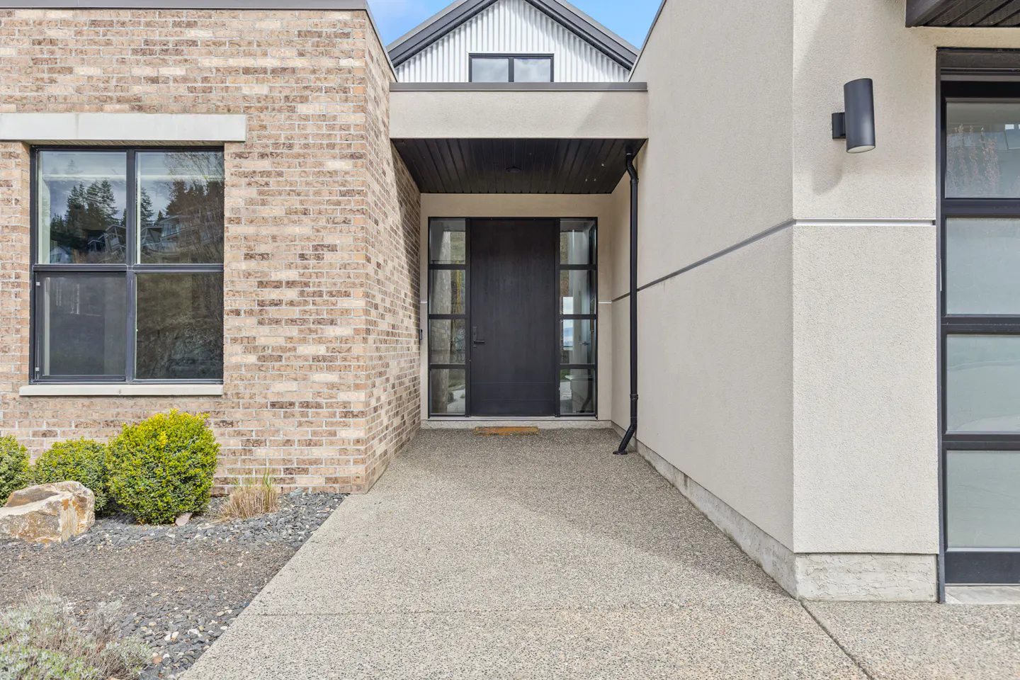 Modern home exterior with a black front door, brick and stucco walls, and a concrete walkway.