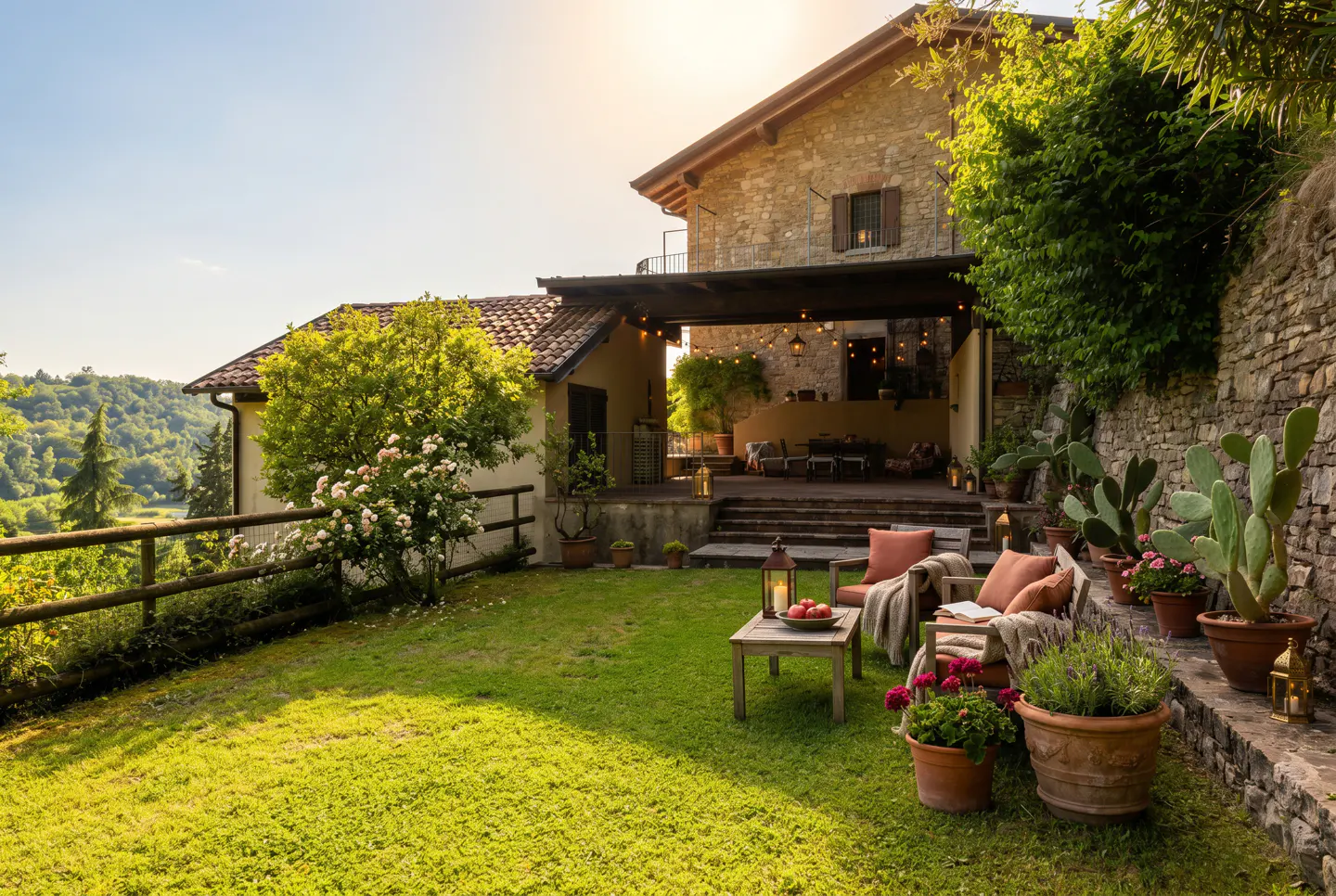 A rustic stone house with a patio, garden seating, potted cacti, and a lush green lawn overlooking a forested valley.