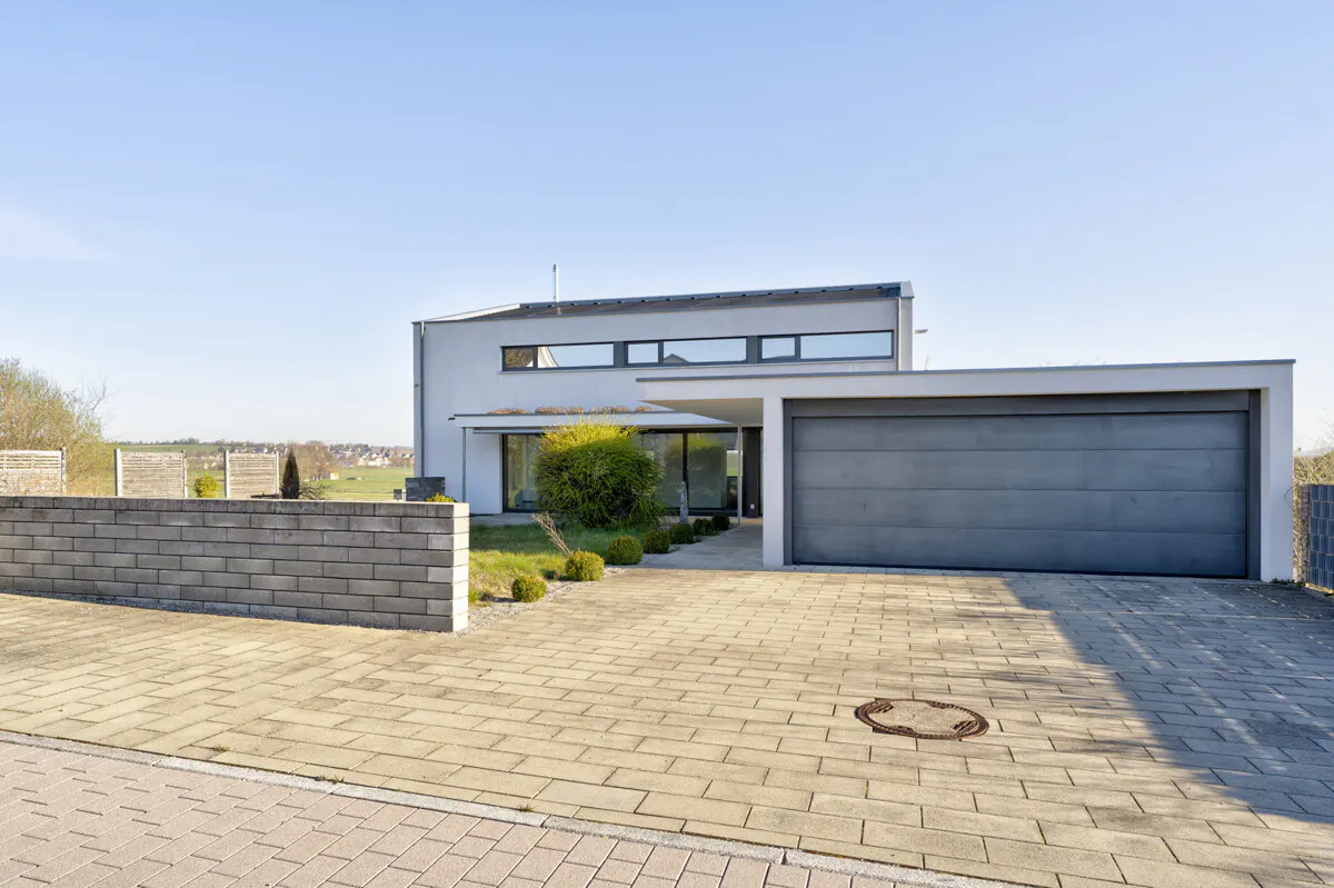 Modern white house with a gray garage door and a stone driveway on a sunny day.