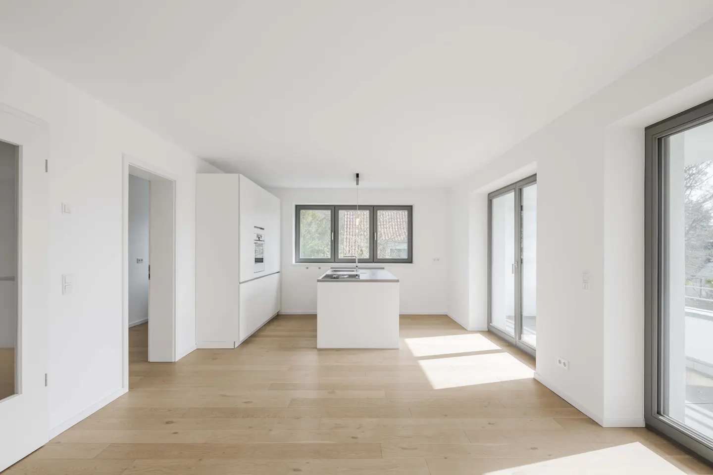Bright, modern kitchen with white cabinets, island, and walls. Light wood floors and large windows with gray frames.