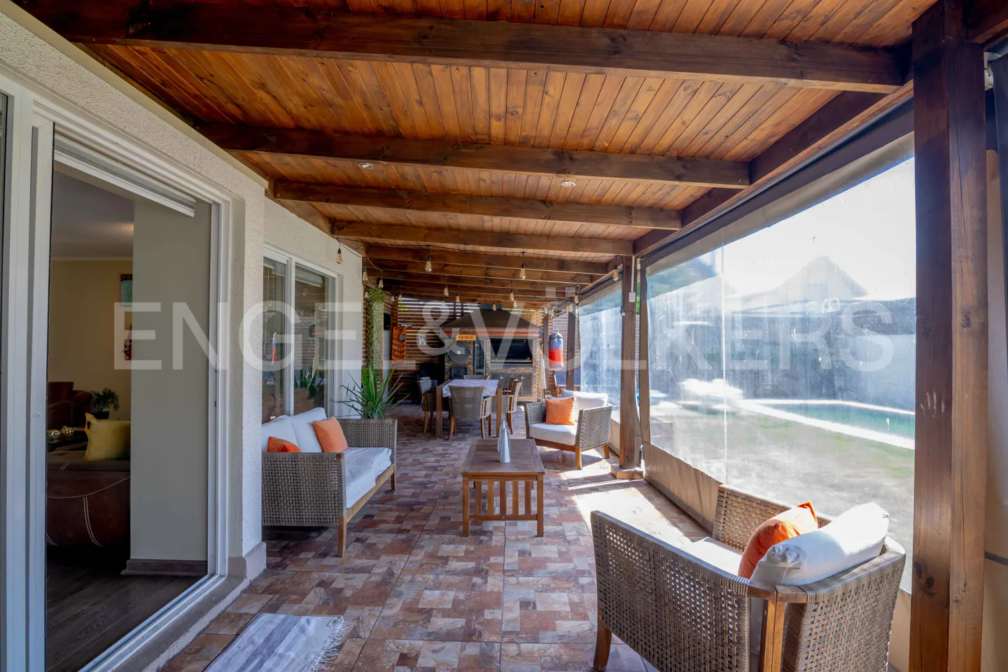 Covered patio with wicker furniture, orange cushions, and a wooden ceiling. A pool is visible in the background.