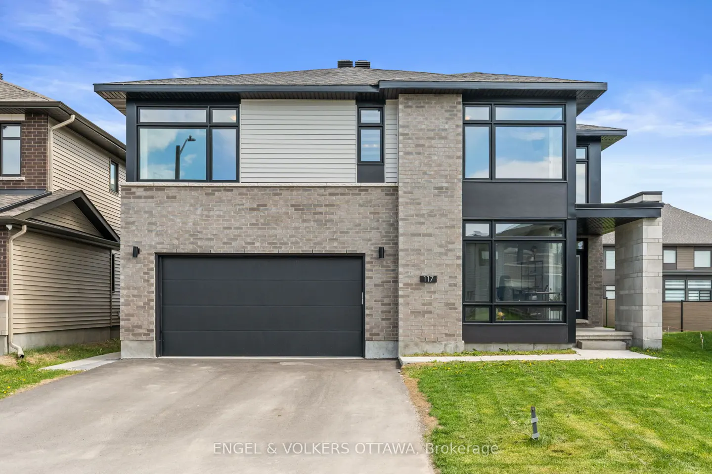 Two-story house with gray brick, gray siding, black trim, and a black garage door on a sunny day.