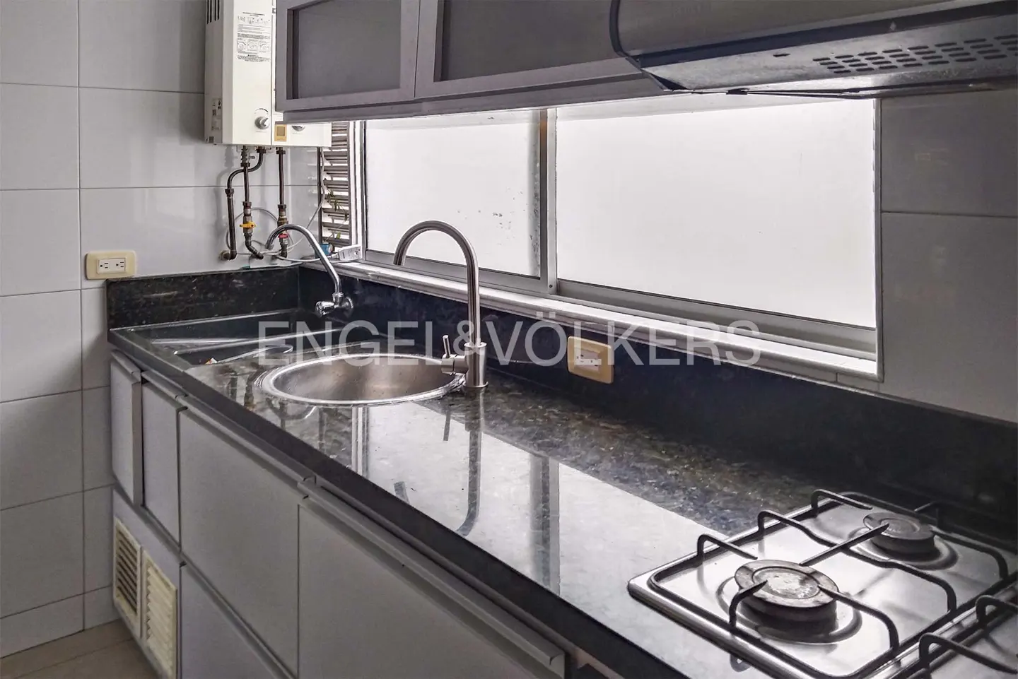 A kitchen with gray cabinets, a black granite countertop, a stainless steel sink, and a two-burner gas stove.