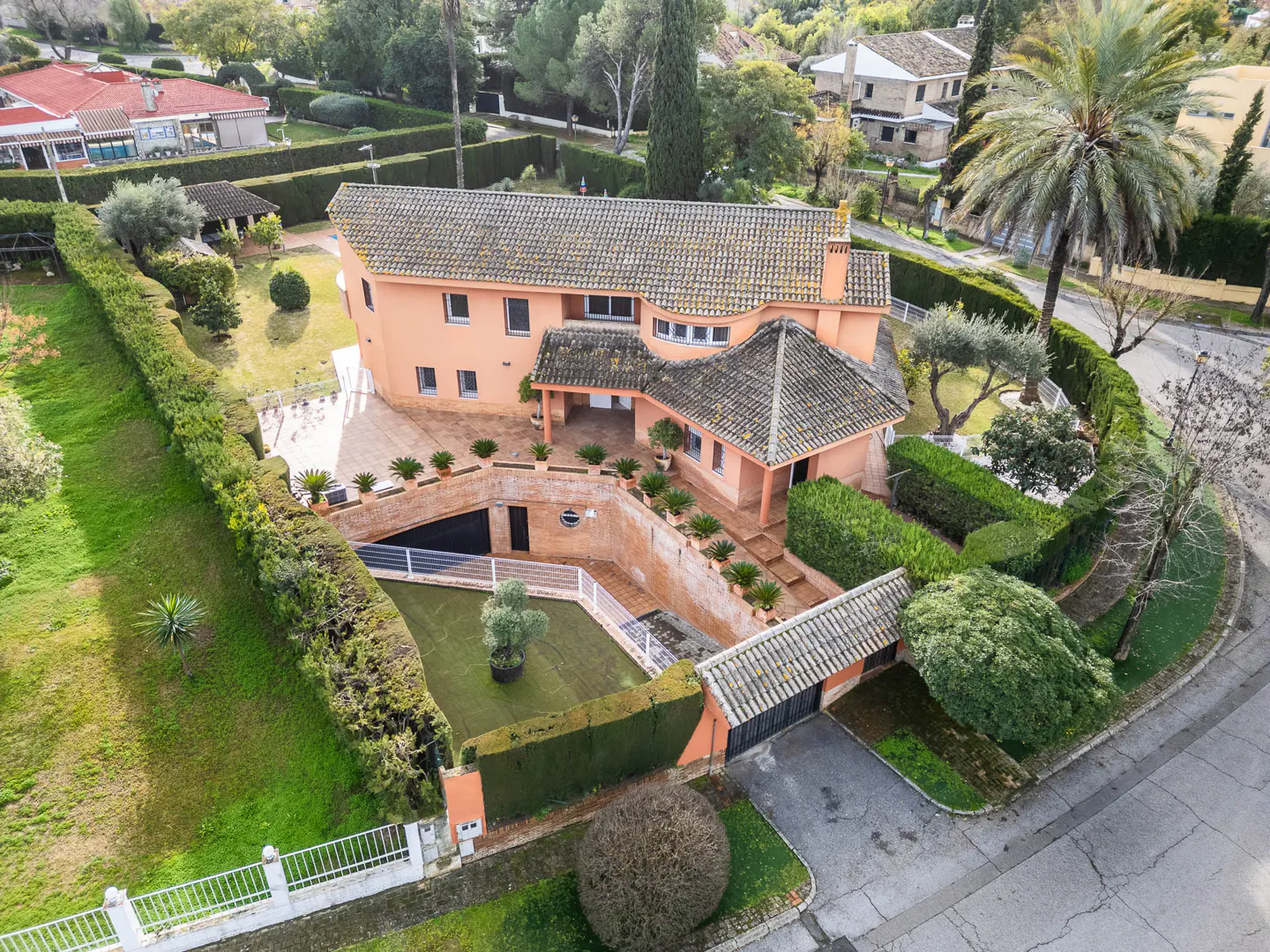 Aerial view of a salmon-colored two-story house with a tiled roof, surrounded by manicured hedges and green lawns.