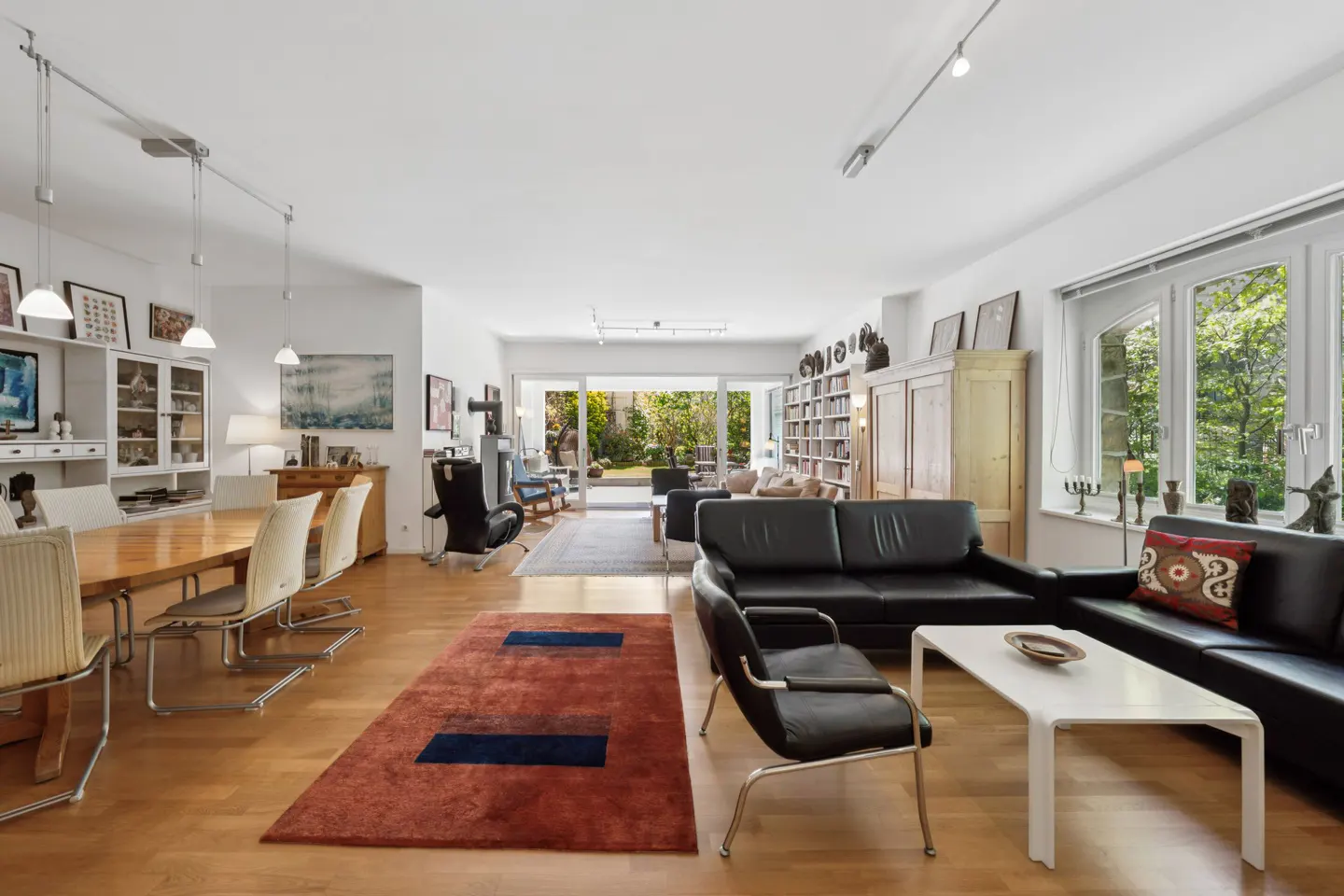 Bright, open-concept living and dining area with hardwood floors, black leather sofas, and a view of the garden through sliding glass doors.