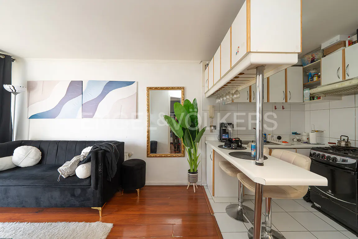 Living room and kitchen area with a black sofa, wood floors, and white cabinets.