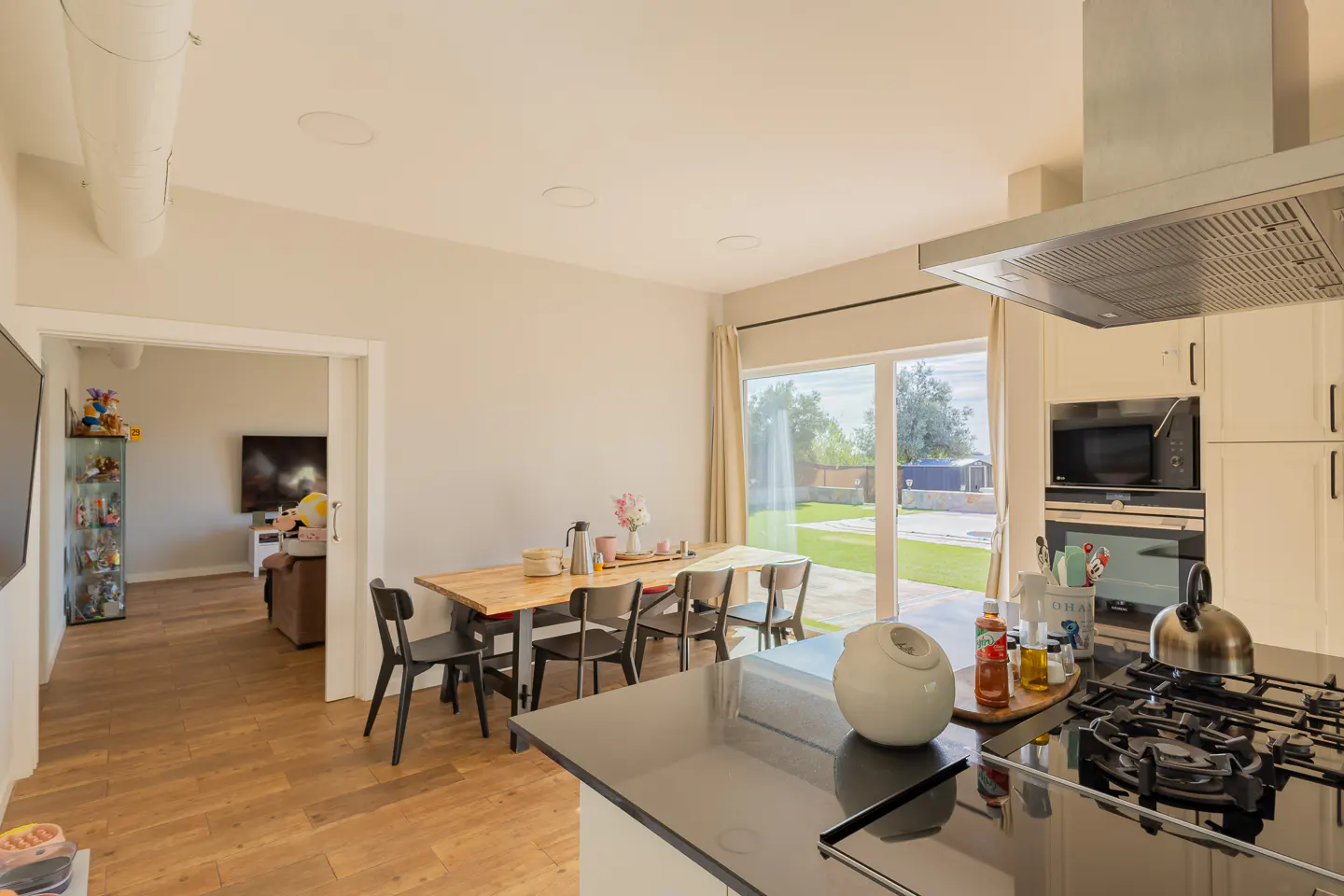 Bright, modern kitchen with wood floors, a dining table, and a view to the backyard through large sliding glass doors.