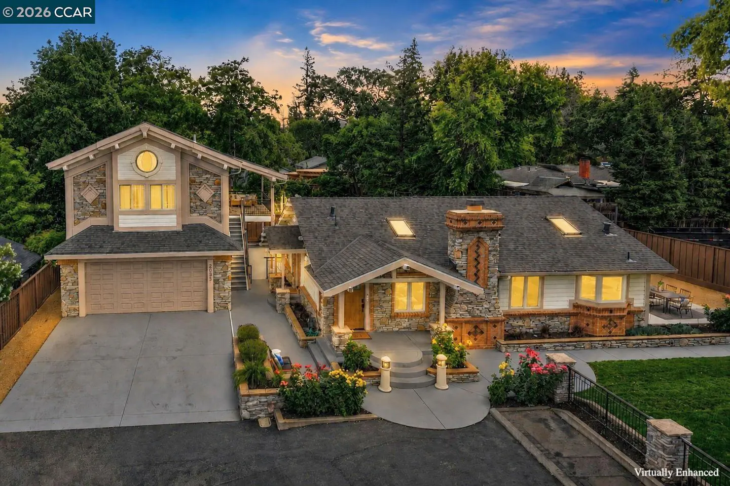 Exterior view of a two-story house with stone accents, a gray roof, and a driveway, surrounded by trees under a blue and orange sky.