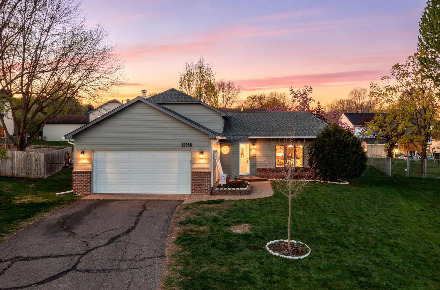 Exterior shot of a one-story house with gray siding, a white garage door, and a green lawn at sunset.