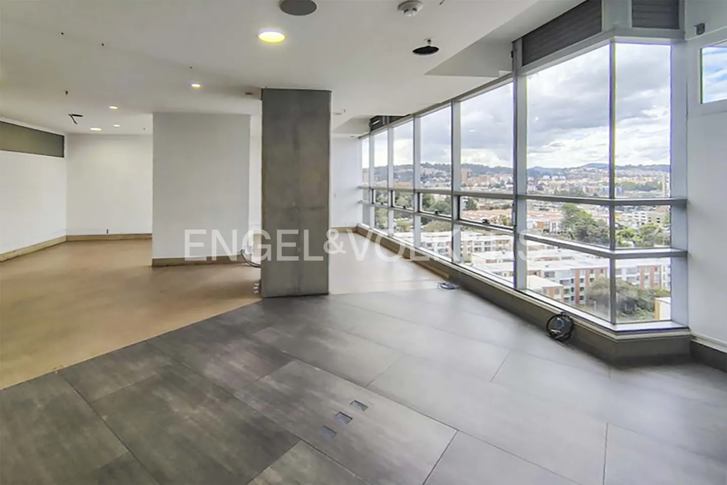 An empty, modern office space with gray floors and floor-to-ceiling windows overlooking a city.