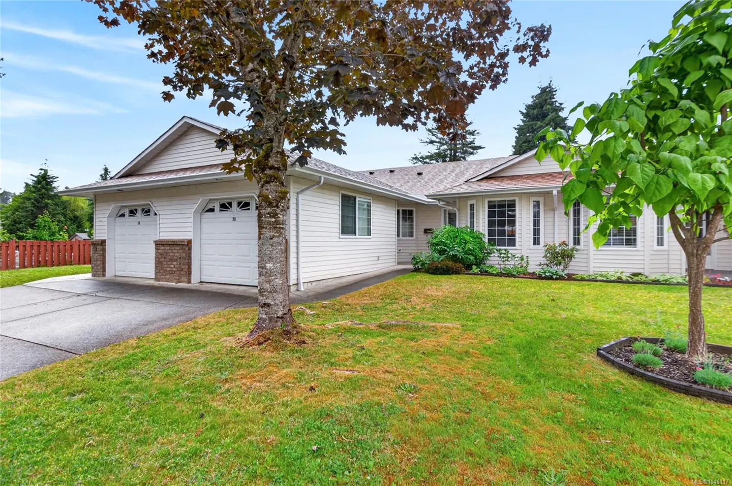 Single-story white house with a two-car garage, concrete driveway, and a green lawn under a blue sky.