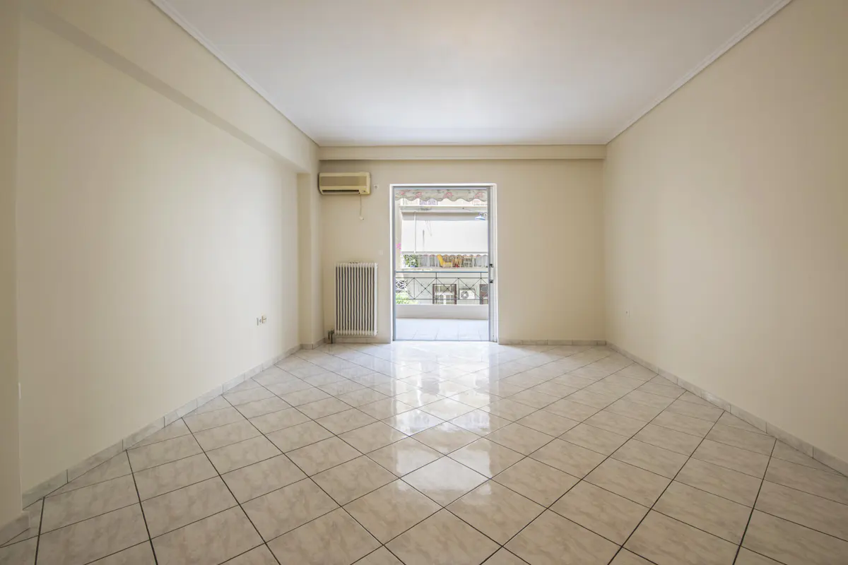 Empty room with beige walls, tiled floor, wall-mounted heater, air conditioner, and a glass door leading to a balcony.