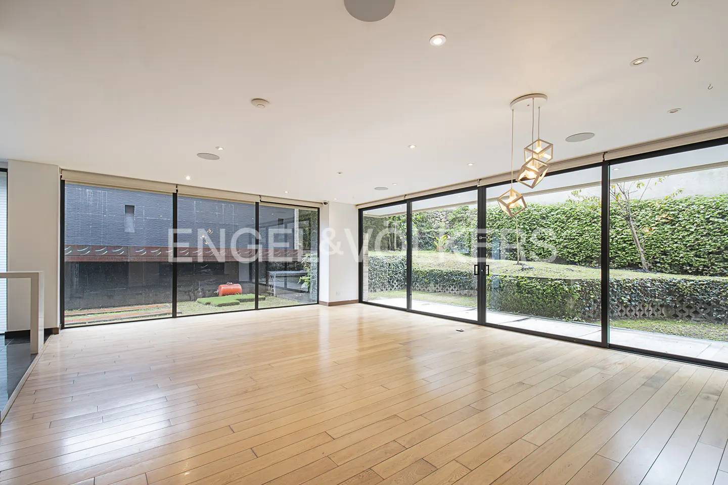 Bright, empty room with light wood floors and large sliding glass doors to a green yard. Modern cube chandelier hangs from the white ceiling.