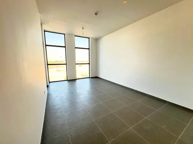 Empty room with white walls, gray tile floor, and two large windows with a view.