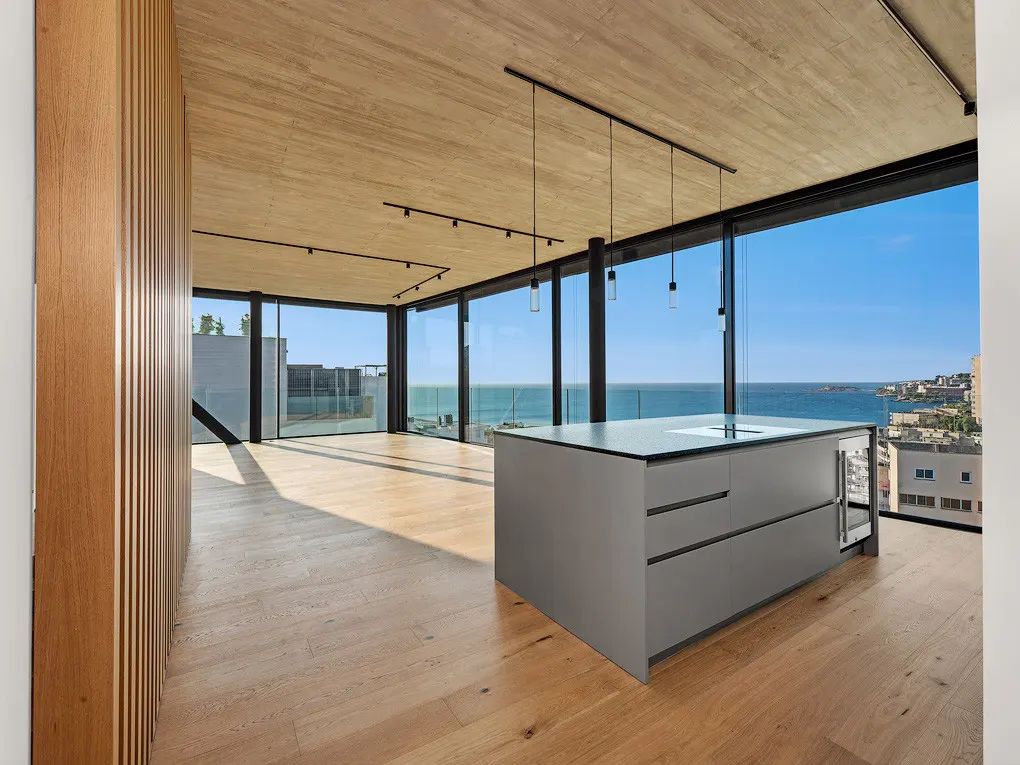 Modern kitchen with a gray island, wood floors, and floor-to-ceiling windows overlooking the ocean.