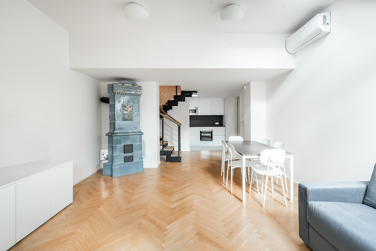 Modern living room with herringbone wood floors, a blue tiled fireplace, dining area, and open kitchen with stairs. [AI-generated text]