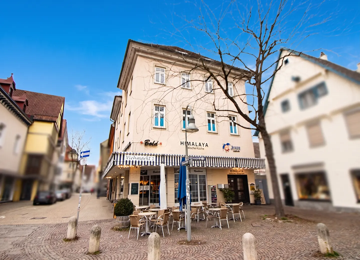 Street view of a three-story beige building with "Himalaya" restaurant signage and outdoor seating under a blue and white striped awning.
