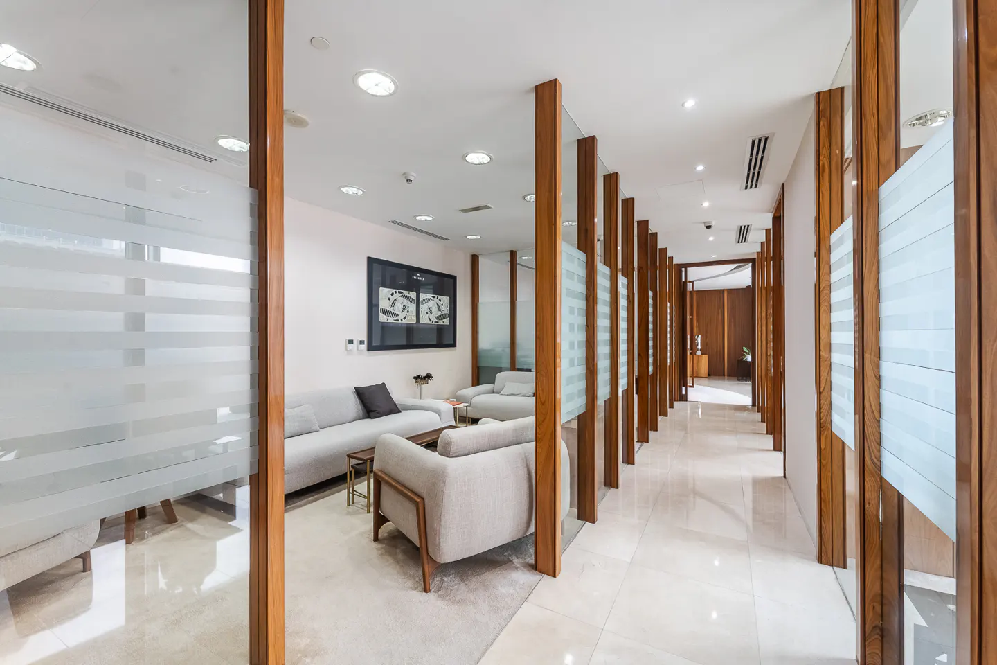 Modern office lobby with light gray sofas, wood dividers with frosted glass, and a white tile floor.