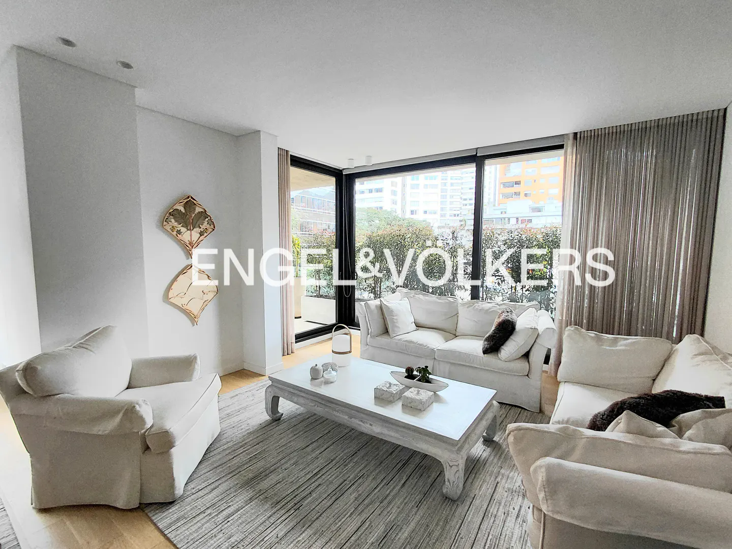 Bright living room with white furniture, a large window with city views, and decorative wall art.
