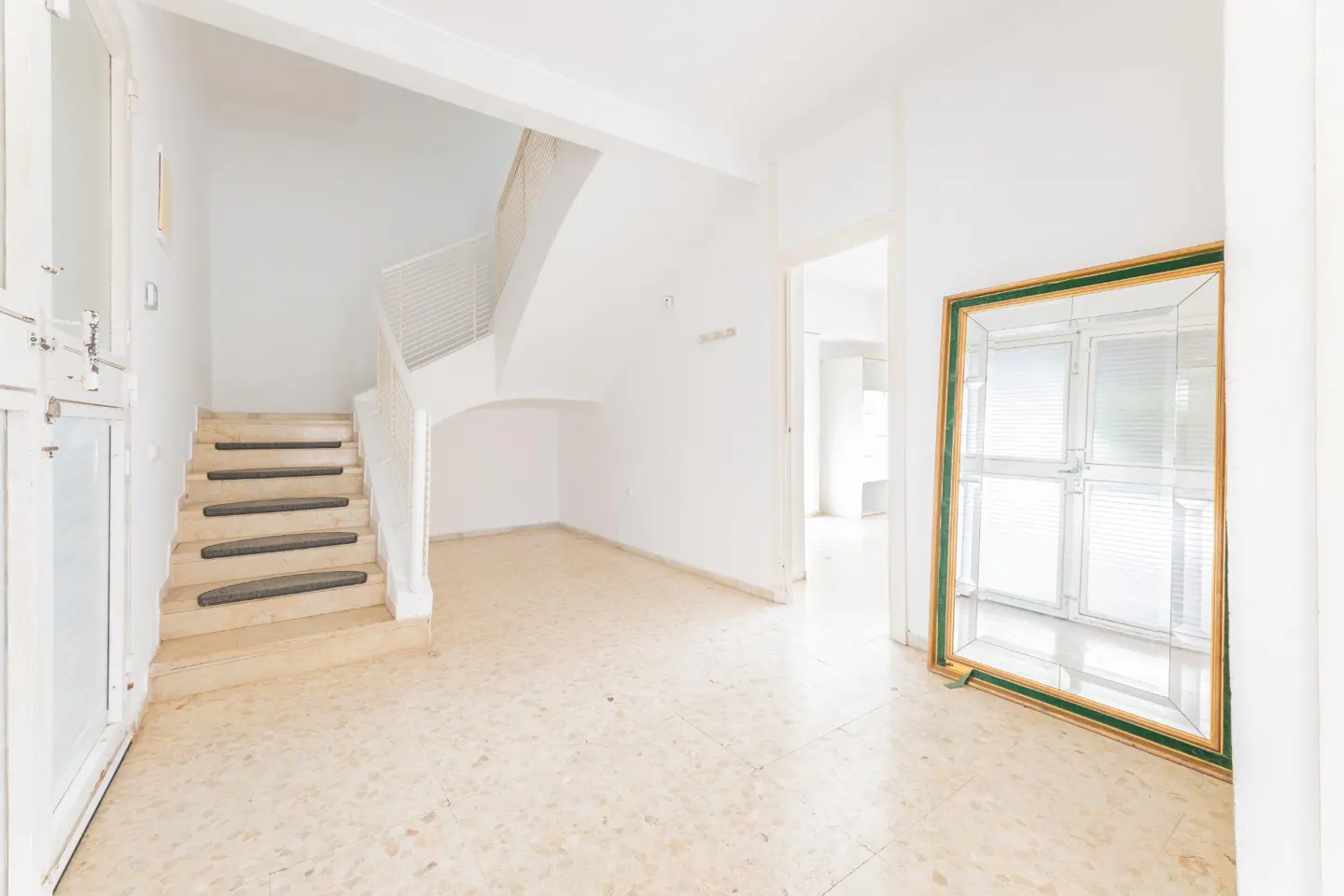 Bright, airy foyer with marble floors, white walls, and a staircase. A large mirror with a gold and green frame leans against the wall.