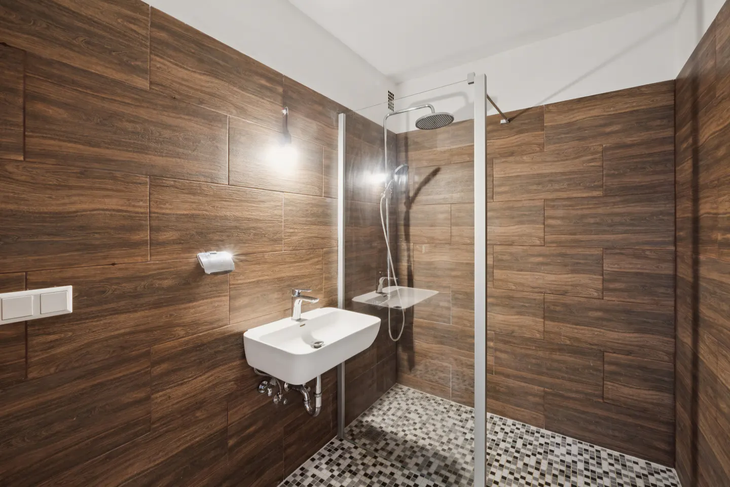 Bathroom with wood-look tile walls, mosaic tile floor, glass shower, and a white sink.