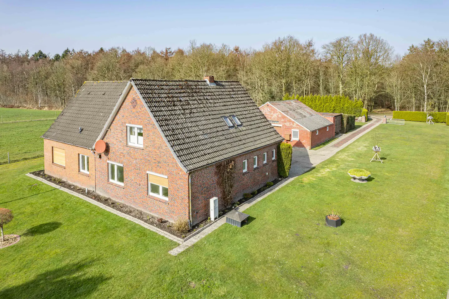 Aerial view of a red brick house with a gray roof, surrounded by a green lawn and trees.
