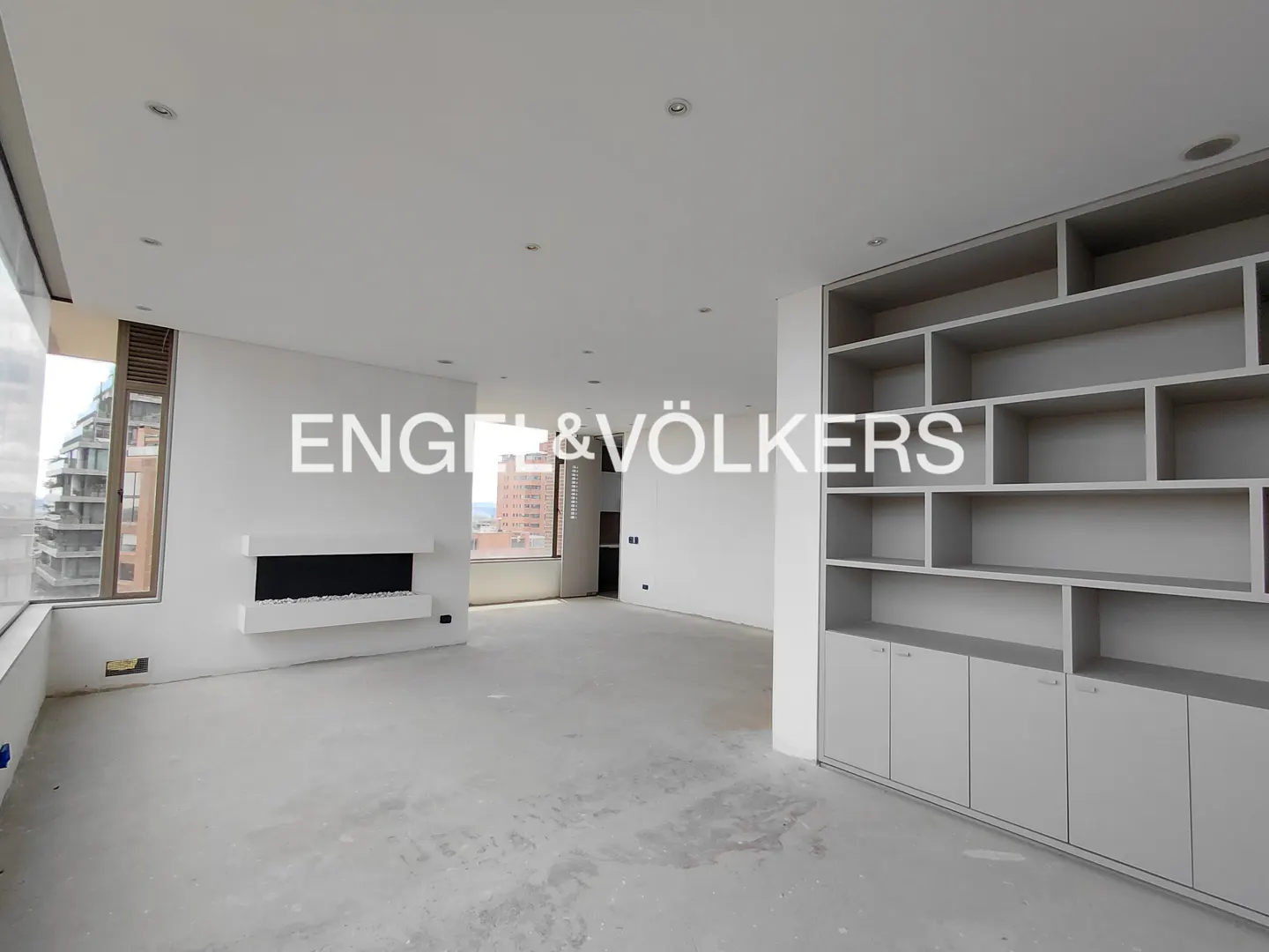 A bright, empty room with a fireplace, built-in shelves, and a large window with a city view.