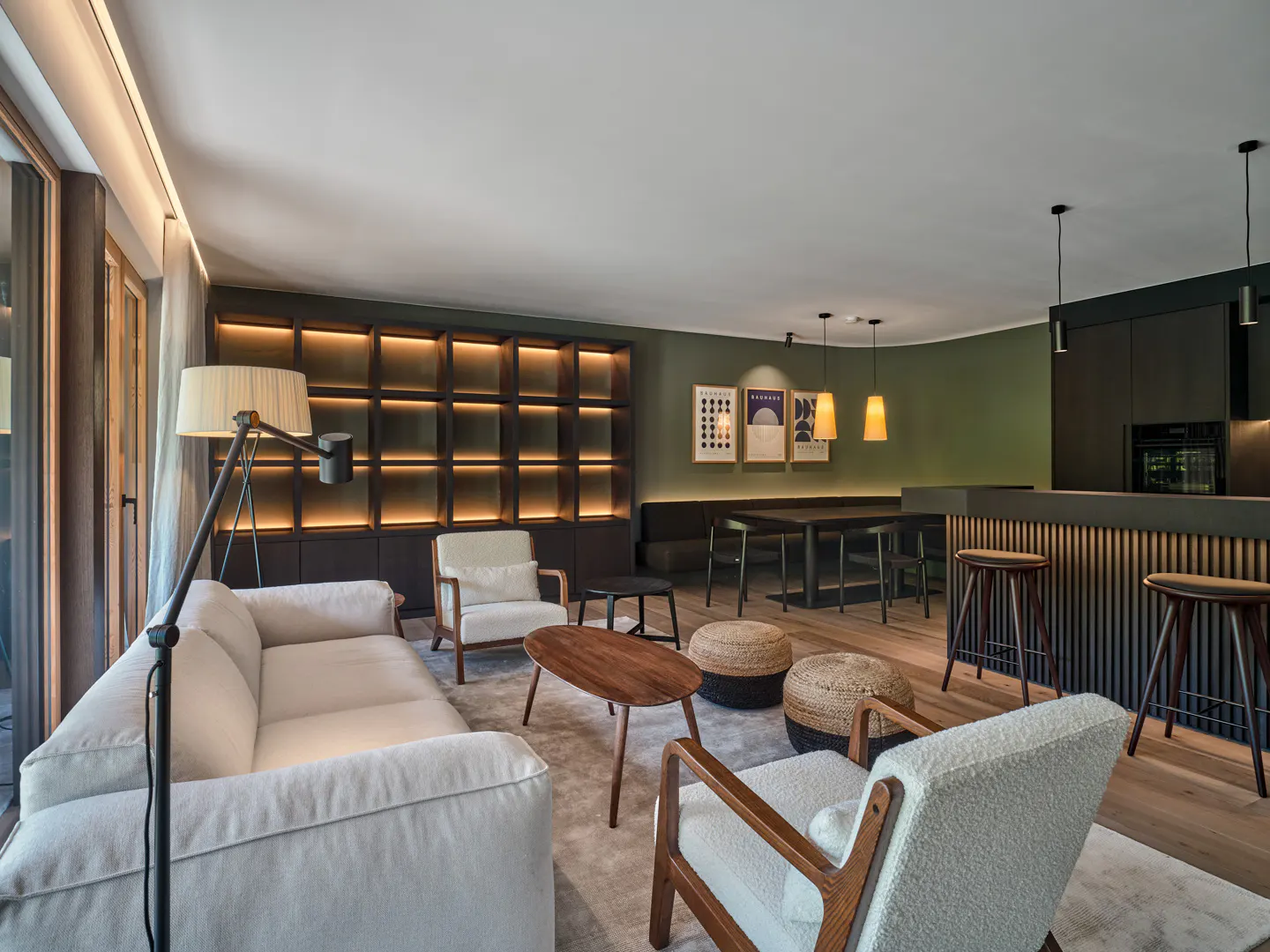 Modern living room with a white sofa, two armchairs, a wooden coffee table, woven ottomans, and a dark kitchen island.