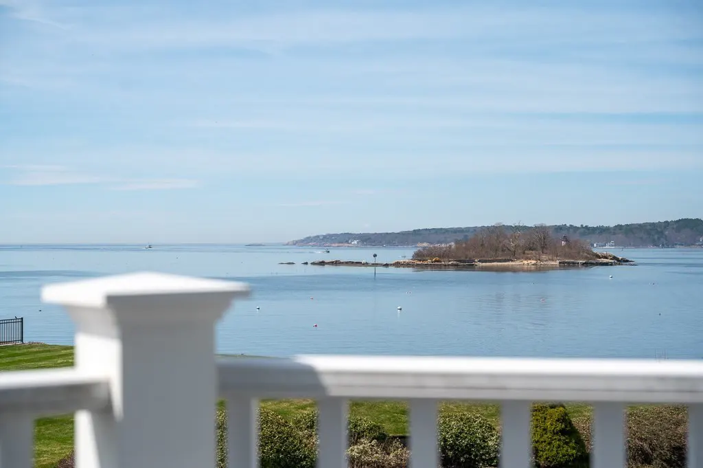 View from a white porch railing overlooking a calm blue bay with a small island in the distance.