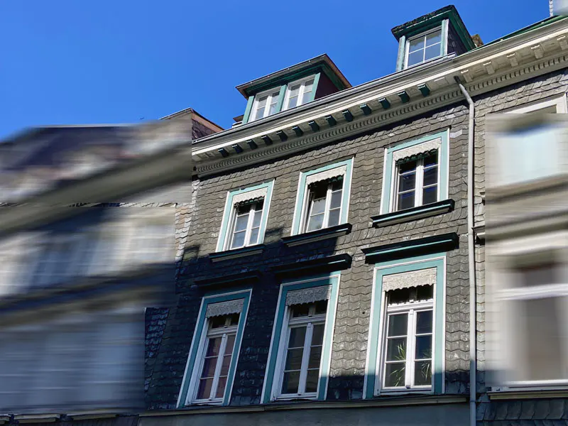 Exterior of a gray stone building with white framed windows and blue trim under a blue sky.