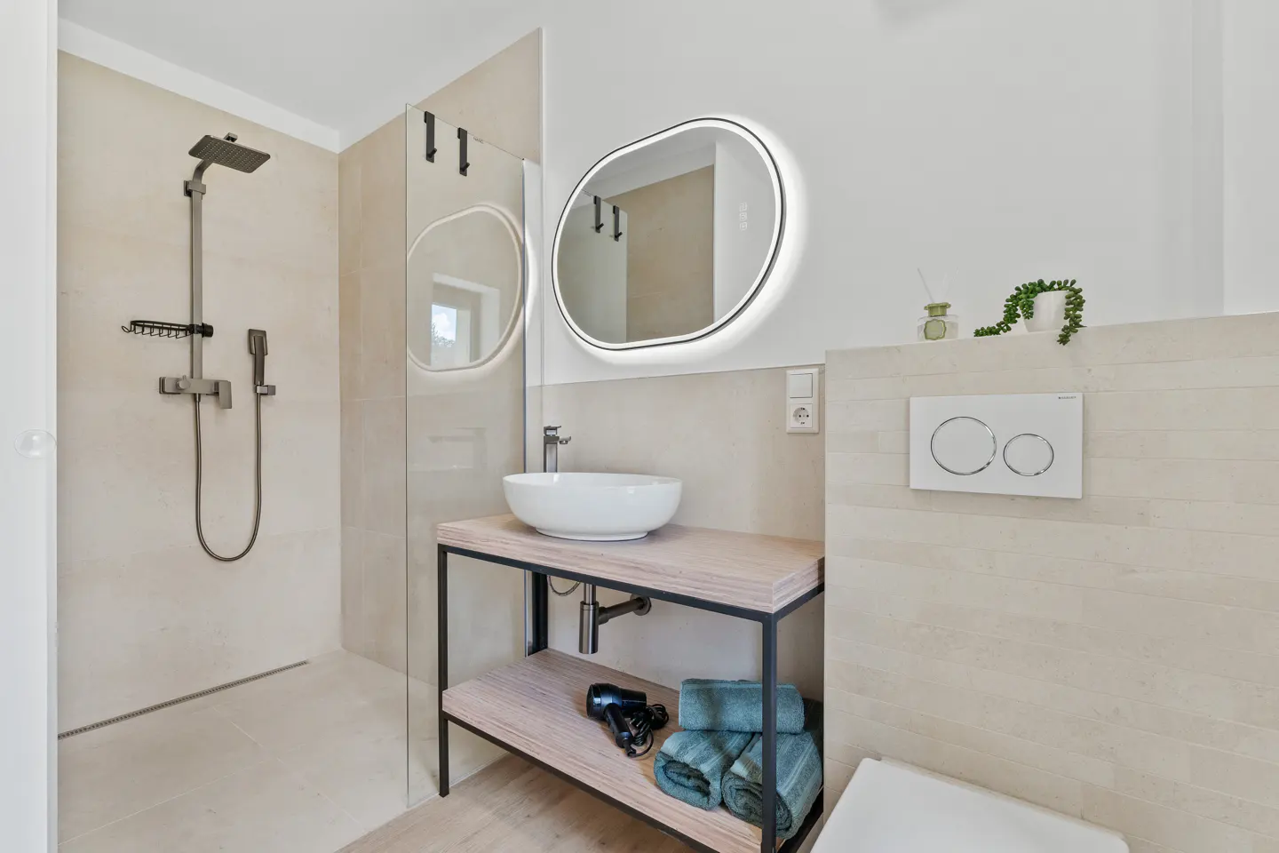Bright bathroom with a shower, sink, and toilet. The sink is white and round, and the mirror is oval with a light.