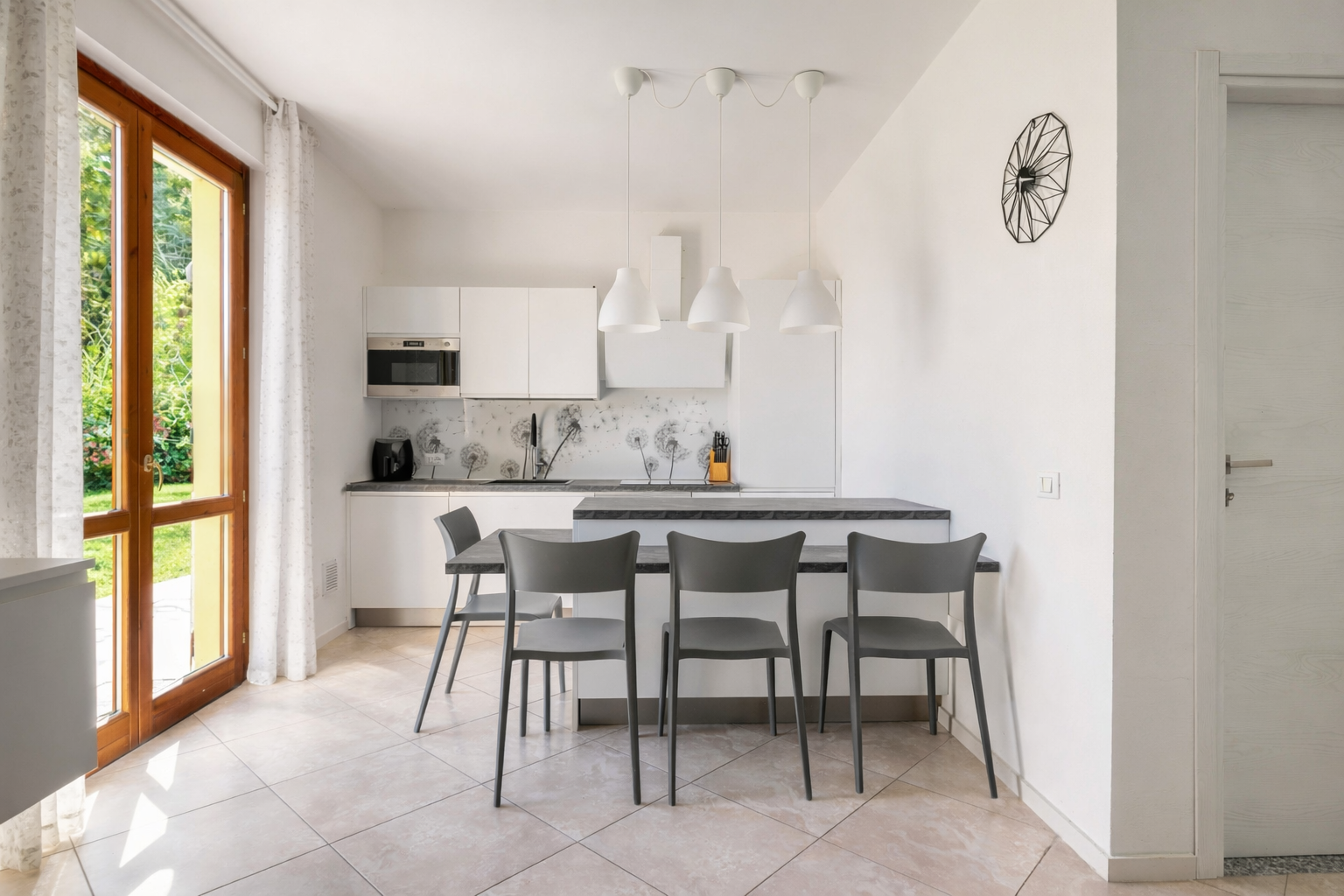 Bright, modern kitchen with white cabinets, gray chairs at a dark countertop island, and a wood-framed glass door to a green garden.