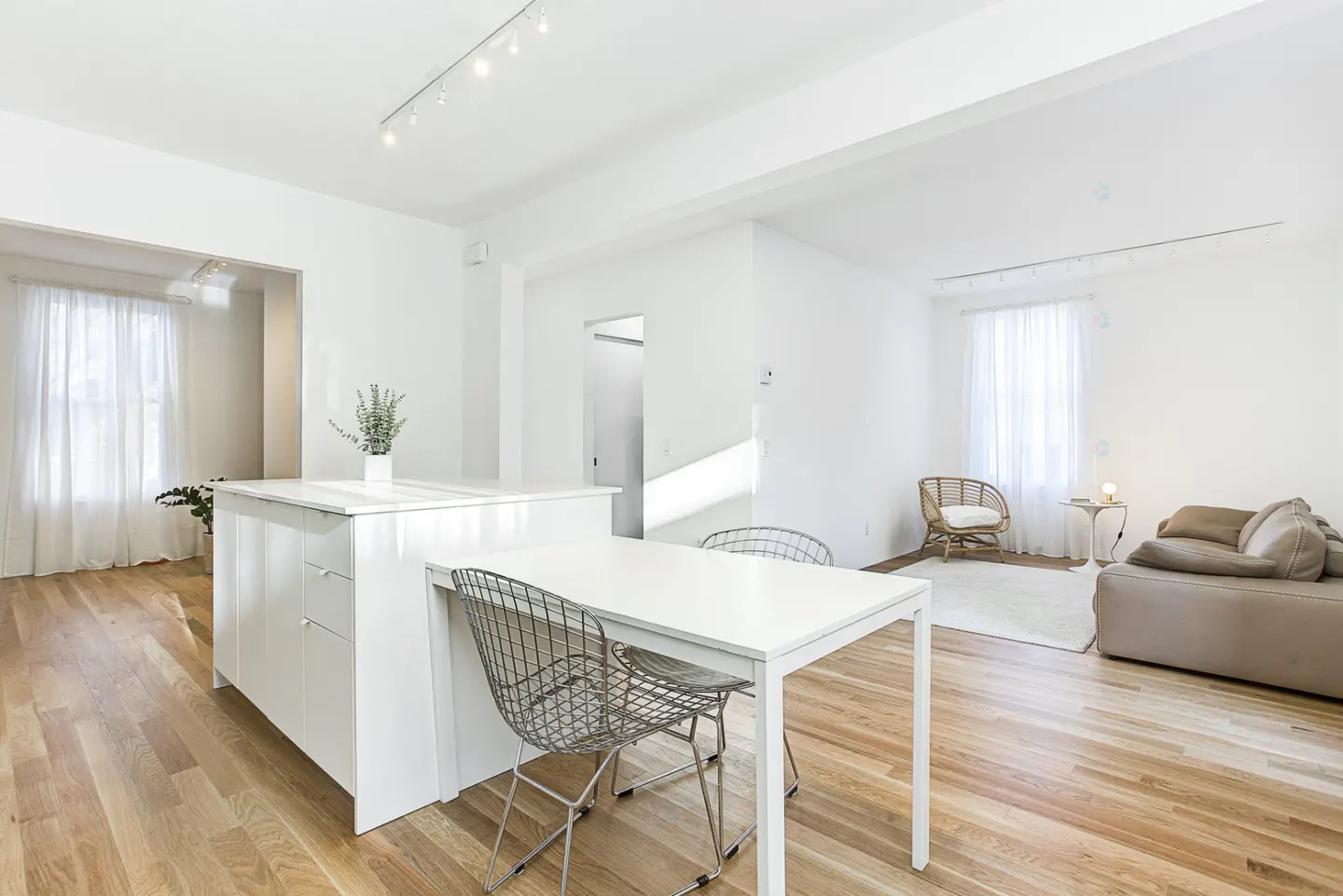 Bright, open-concept living space with white walls, wood floors, and natural light. Features a kitchen island, dining table, and cozy seating area.