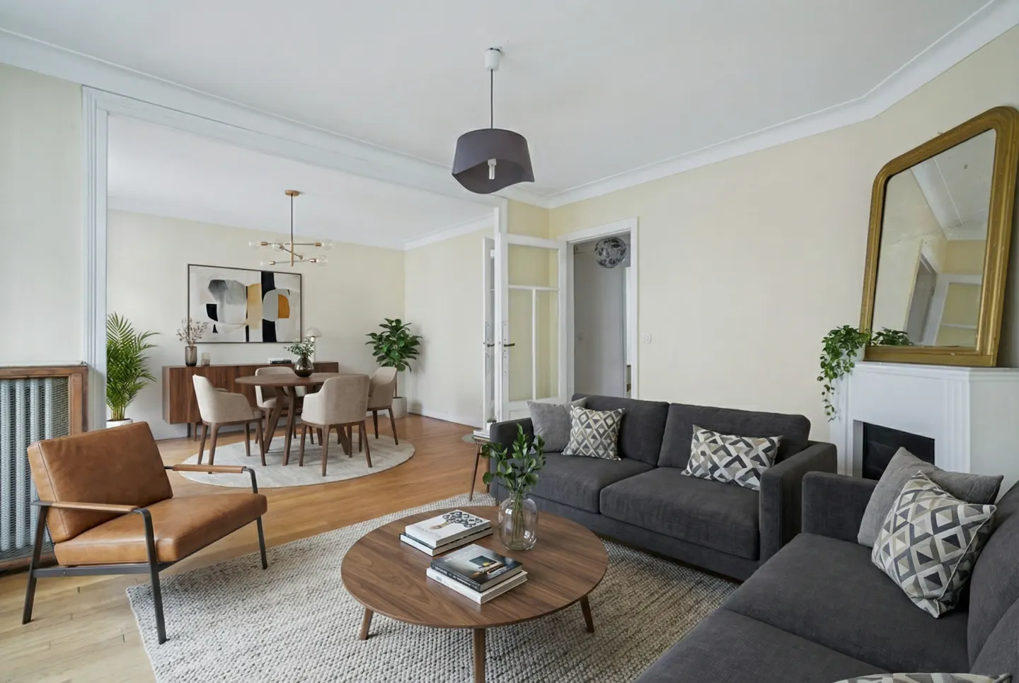 A living and dining room with a gray sofa, round wood table, and a dining table with four chairs.