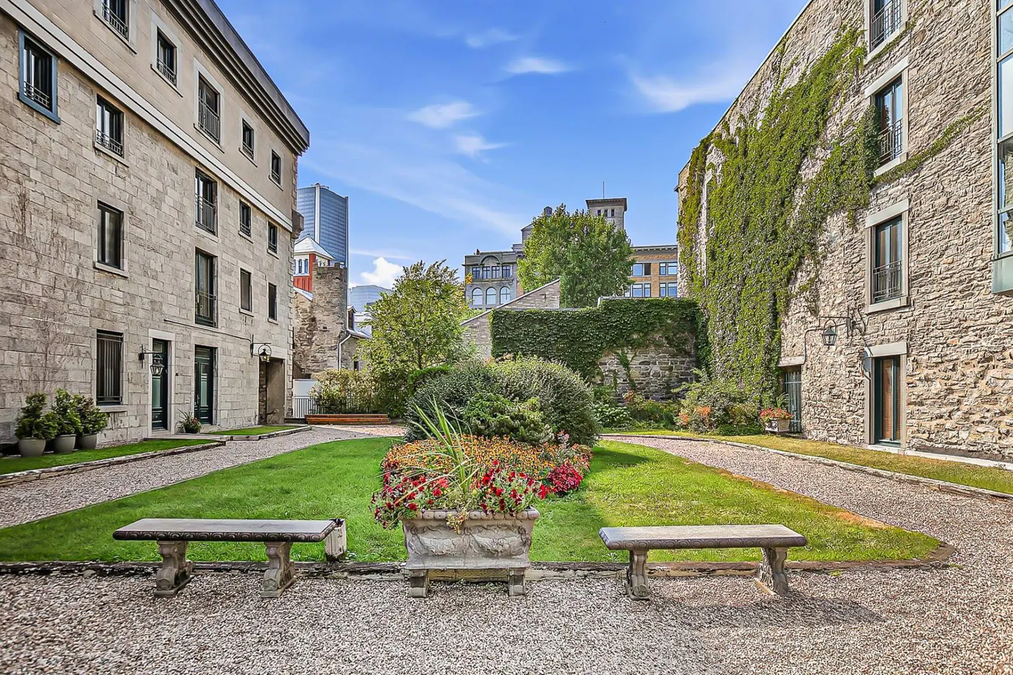 Stone courtyard with benches, flowers, and ivy-covered walls under a blue sky.