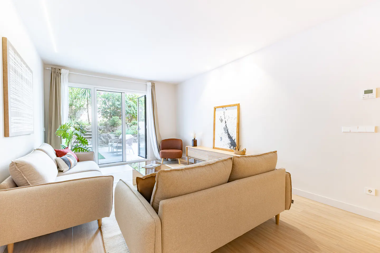 Bright living room with two beige sofas, a wooden console, an orange armchair, and glass doors opening to a garden.