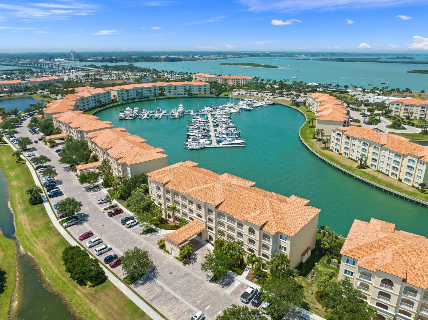 Aerial view of waterfront condos with terracotta roofs surrounding a marina filled with boats on a sunny day.
