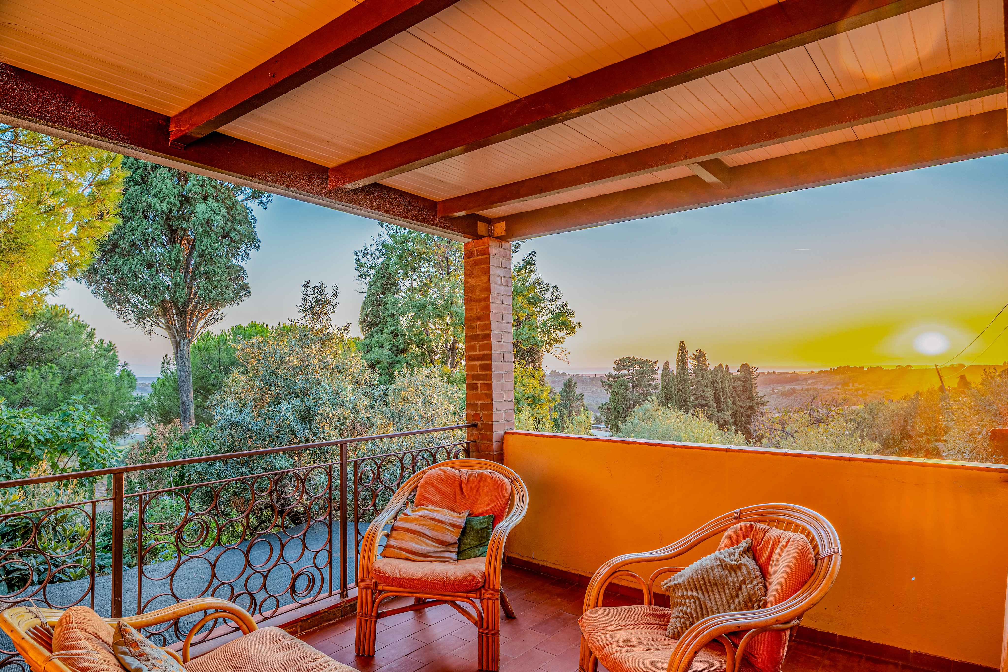 Covered balcony with wicker chairs overlooking a scenic sunset over trees and rolling hills. [AI-generated text]