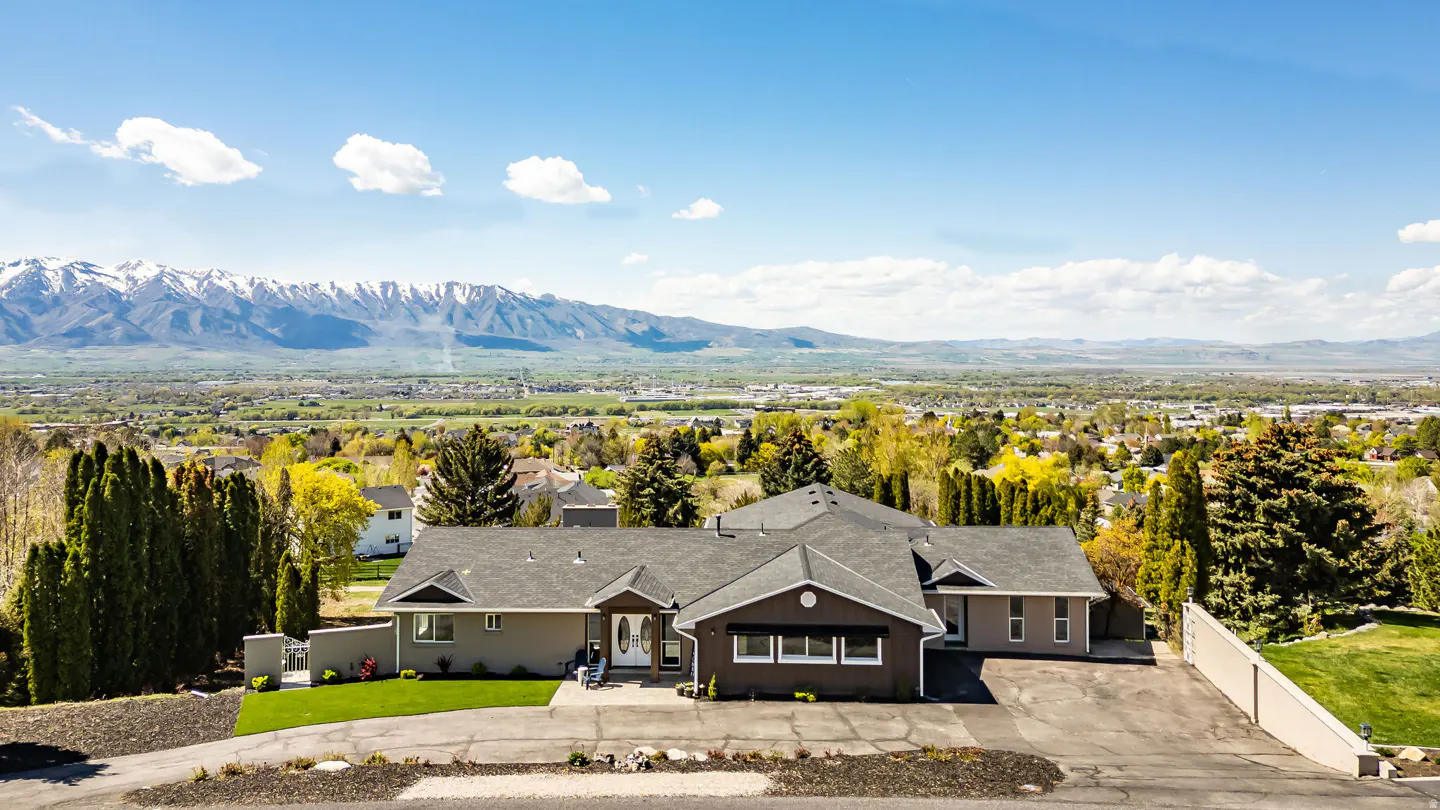 A single-family home with a gray roof and siding, a green lawn, and a mountain range in the background.
